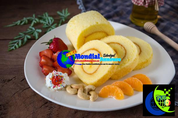 Sponge cake roll with cream, strawberries and orange fruits on a white plate on wooded table background. Rouleau à l'Orange